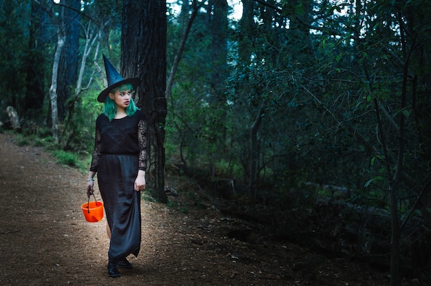 Joven bruja con cesta de pie en el bosque