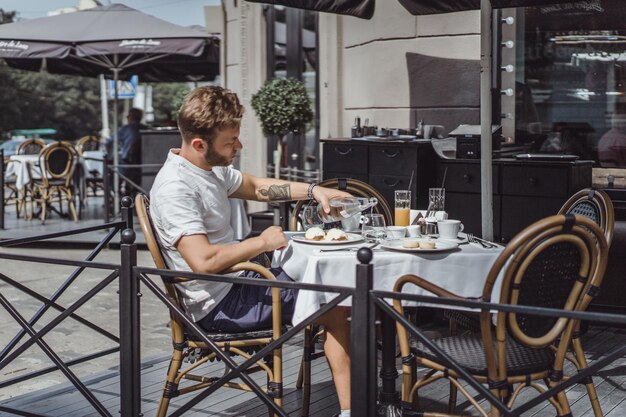 un joven en un café de verano en la terraza desayuna