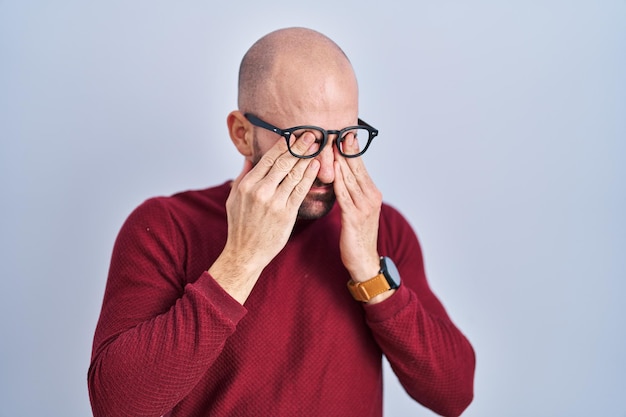 Foto gratuita joven calvo con barba sobre fondo blanco con gafas frotándose los ojos por fatiga y dolor de cabeza, expresión soñolienta y cansada. problema de visión