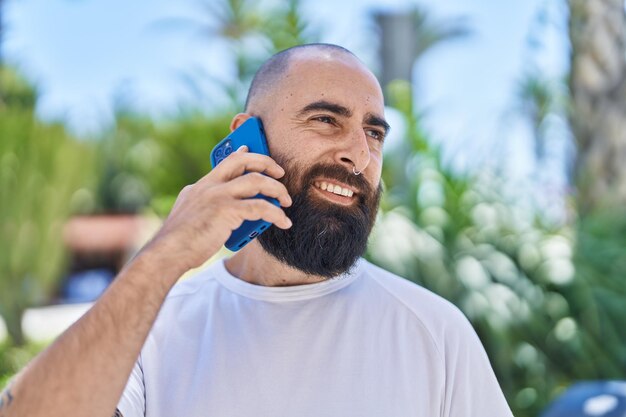 Joven calvo sonriendo confiado hablando por teléfono inteligente en el parque