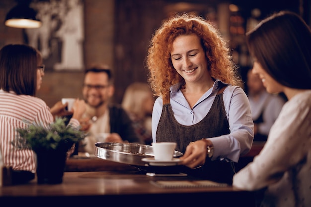 Joven camarera feliz dando café a una invitada mientras trabaja en un bar