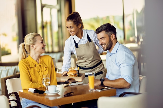 Joven camarera feliz sirviendo comida a los invitados en un restaurante