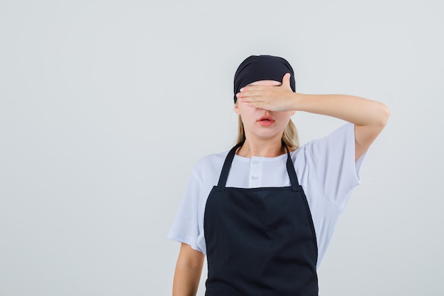 Foto gratuita joven camarera que cubre los ojos con la mano en uniforme y delantal