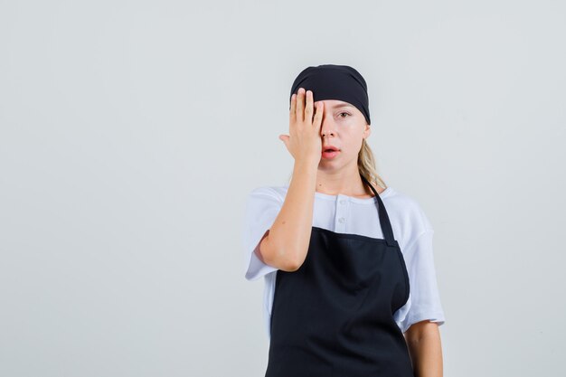 Joven camarera que cubre los ojos con la mano en uniforme y delantal