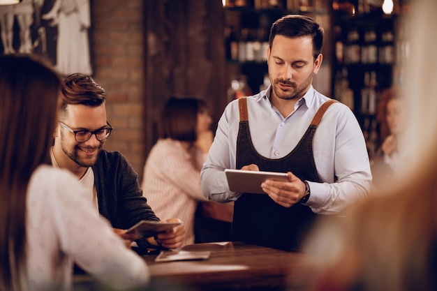 Foto gratuita joven camarero escribiendo orden en el panel táctil mientras atiende a los invitados en un bar