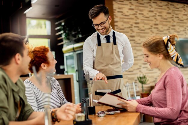 Joven camarero feliz comunicándose con un grupo de clientes en un café