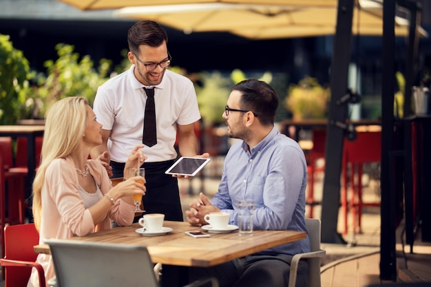 Joven camarero feliz comunicándose con los invitados en un café al aire libre