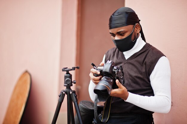 Joven camarógrafo afroamericano profesional con cámara profesional con equipo profesional Camarógrafo afro con duraq negro y máscara de protección facial haciendo videos