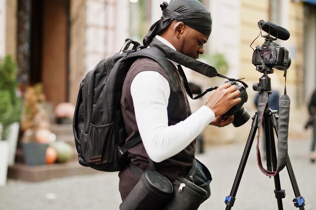 Joven camarógrafo afroamericano profesional con cámara profesional con equipo profesional de trípode Camarógrafo afro vestido con duraq negro haciendo videos