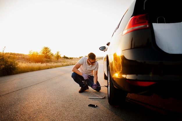 Joven cambiando la rueda del coche