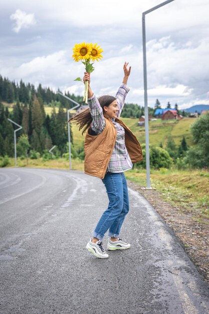 Una joven camina por las montañas con un ramo de girasoles.