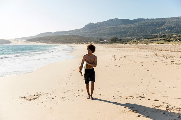 Joven caminando por la orilla del mar con tabla de surf