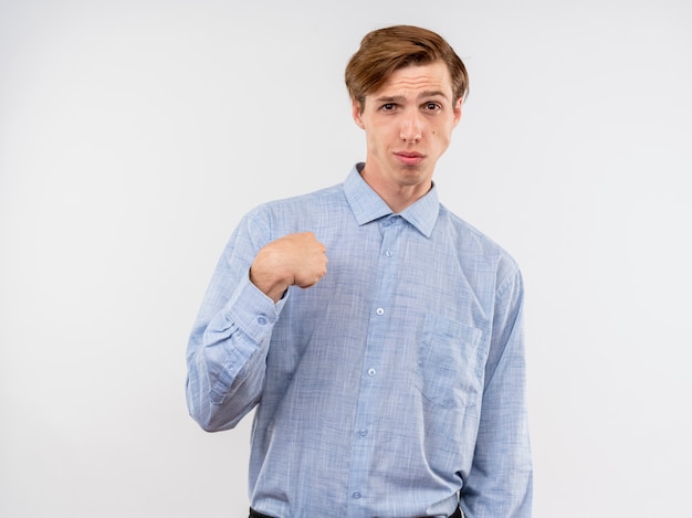 Joven con camisa azul mirando a la cámara apuntando con el dedo índice a sí mismo mirando confiado de pie sobre fondo blanco.