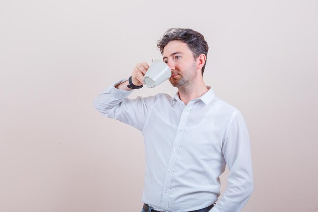 Joven con camisa blanca bebiendo té aromático y mirando pensativo