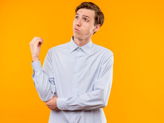 Joven con camisa blanca mirando a un lado desconcertado parado sobre la pared naranja