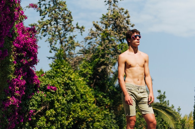 Joven sin camisa con gafas posando en el parque