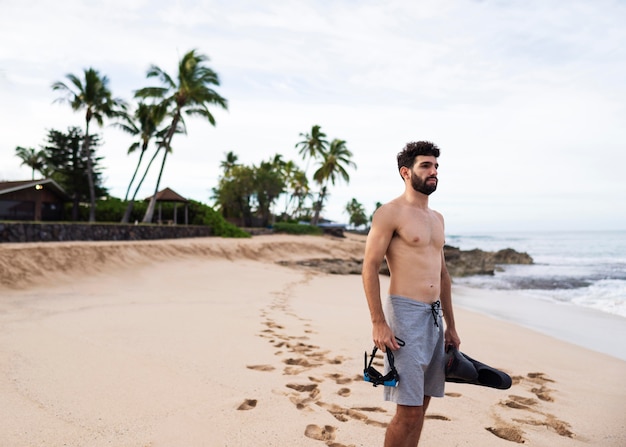 Joven sin camisa en la playa con equipo de buceo