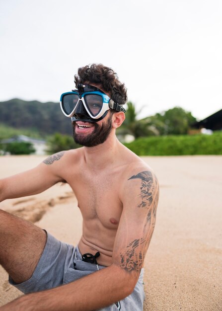 Joven sin camisa en la playa con equipo de buceo