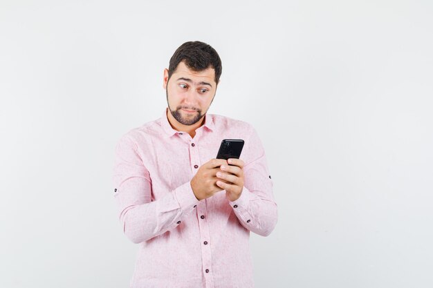 Joven en camisa rosa con teléfono móvil y mirando sorprendido