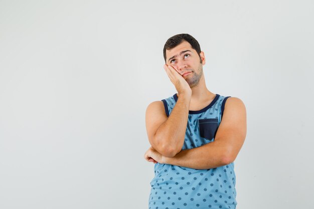 Joven en camiseta azul apoyándose en la mejilla de la palma levantada y mirando pensativo