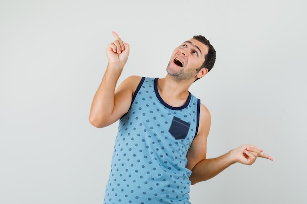 Joven en camiseta azul apuntando con el dedo hacia arriba y hacia abajo y mirando esperanzado