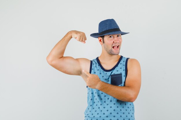 Joven en camiseta azul, sombrero apuntando a los músculos del brazo y luciendo fuerte