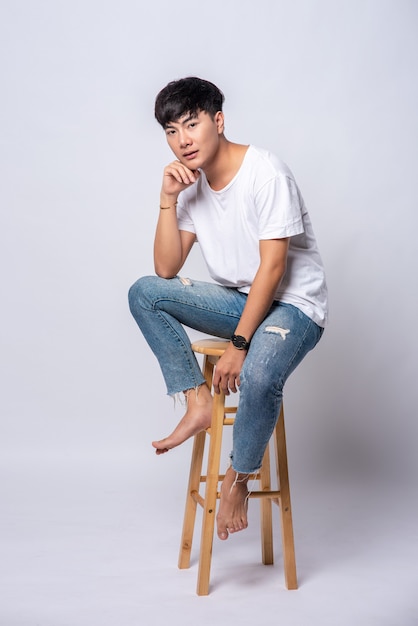 Un joven con una camiseta blanca está sentado en una silla alta.