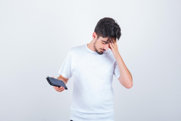 Joven en camiseta blanca sosteniendo billetera y mirando olvidadizo