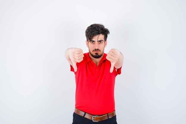 Joven en camiseta roja mostrando los pulgares hacia abajo con ambas manos y mirando serio