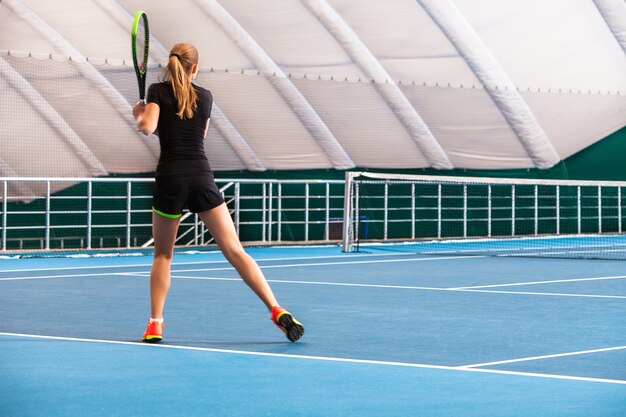 La joven en una cancha de tenis cerrada con pelota y raqueta