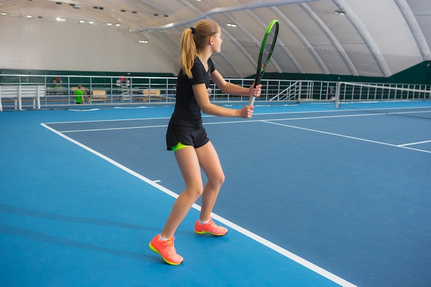 La joven en una cancha de tenis cerrada con pelota