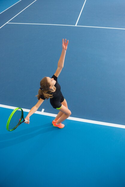 La joven en una cancha de tenis cerrada con pelota