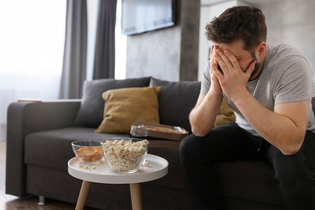 Foto gratuita joven cansado en el sofá de casa sentado junto a la comida chatarra