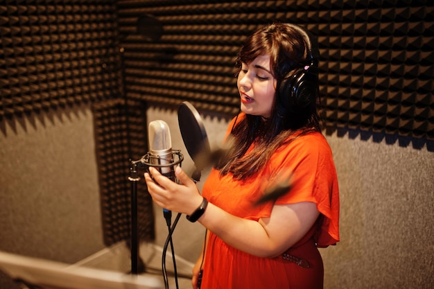 Joven cantante asiática con micrófono grabando una canción en un estudio de grabación de música