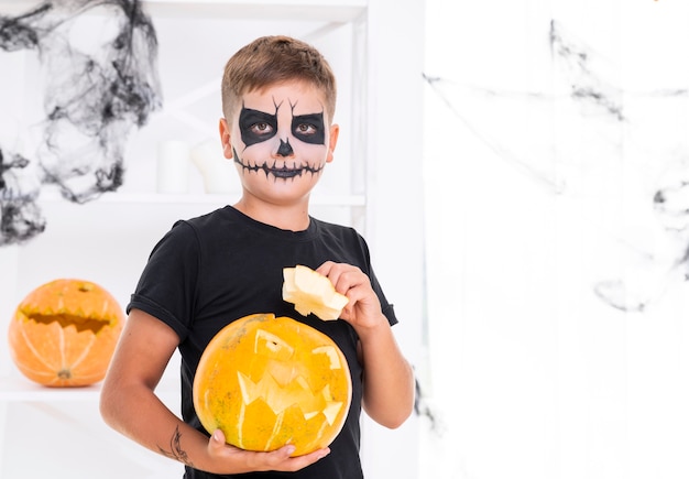 Foto gratuita joven con la cara pintada sosteniendo una calabaza