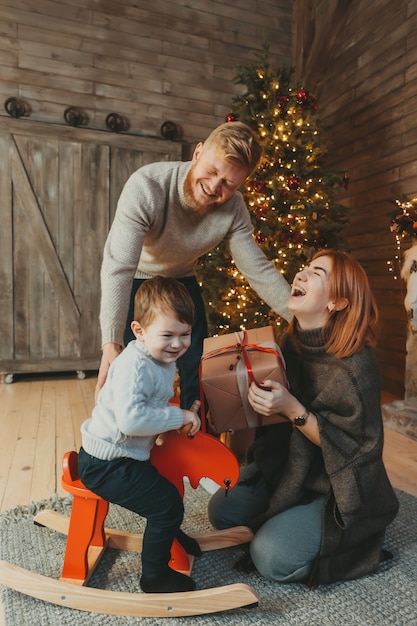 Joven caucásica familia mamá papá hijo cerca de chimenea árbol de navidad