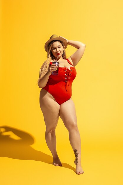 Joven caucásica modelo femenino de talla grande se prepara para resort de playa en amarillo