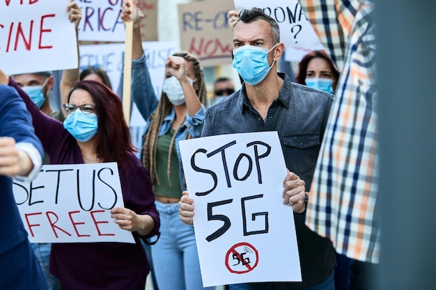 Joven caucásico que lleva una pancarta con Stop 5G mientras protesta con una multitud de personas durante la epidemia de coronavirus