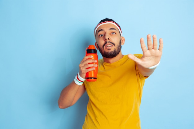 Joven caucásico en ropa brillante entrenando en el espacio azul Concepto de deporte, emociones humanas, expresión facial, estilo de vida saludable, juventud, ventas