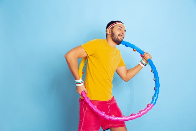 Joven caucásico en ropa brillante entrenando en el espacio azul Concepto de deporte, emociones humanas, expresión facial, estilo de vida saludable, juventud, ventas