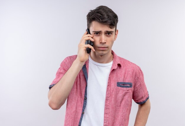 Joven caucásico vestido con camisa rosa habla por teléfono en la pared blanca aislada