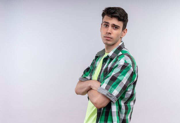 Foto gratuita joven caucásico vestido con camisa verde cruzando las manos sobre la pared blanca aislada