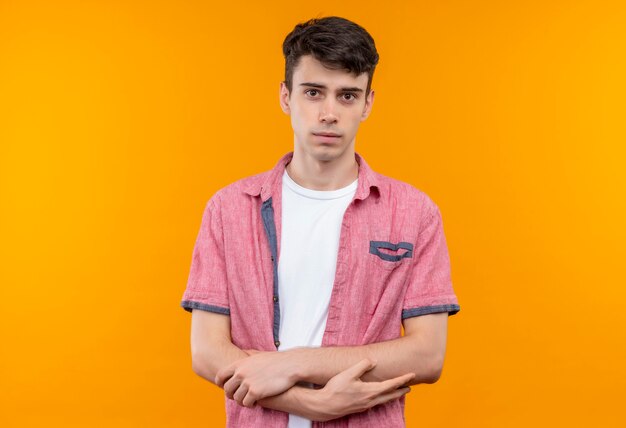 Joven caucásico vistiendo camisa rosa cruzando las manos sobre la pared naranja aislada