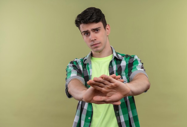 Joven caucásico vistiendo camisa verde mostrando gesto no en pared verde aislada
