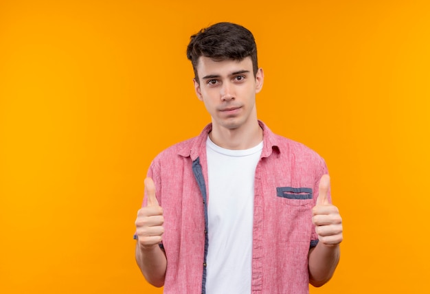 Joven caucásico vistiendo camiseta rosa con los pulgares hacia arriba en la pared naranja aislada