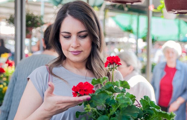 Joven celebración de geranio en olla de barro en el centro de jardinería. Jardinería, plantar - mujer con flores de geranio