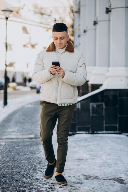 Joven con chaqueta de invierno usando el teléfono fuera de la calle