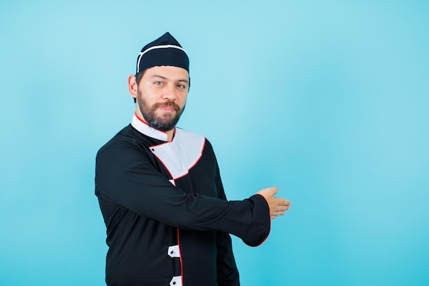 El joven chef está extendiendo su mano hacia atrás sobre fondo azul.