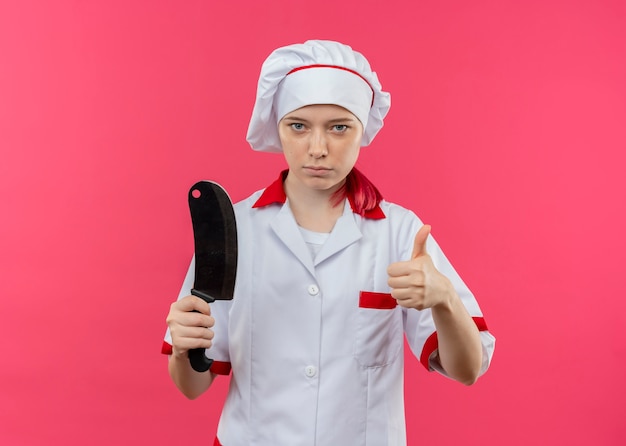 Foto gratuita joven chef mujer rubia segura en uniforme de chef sostiene cuchillo y pulgar hacia arriba aislado en pared rosa