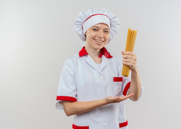 Joven chef mujer rubia sonriente en uniforme de chef tiene manojo de espaguetis aislado en la pared blanca